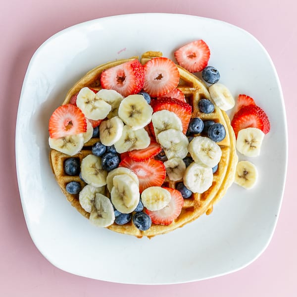 Golden waffle topped with sliced strawberries, blueberries, and bananas on a white plate.