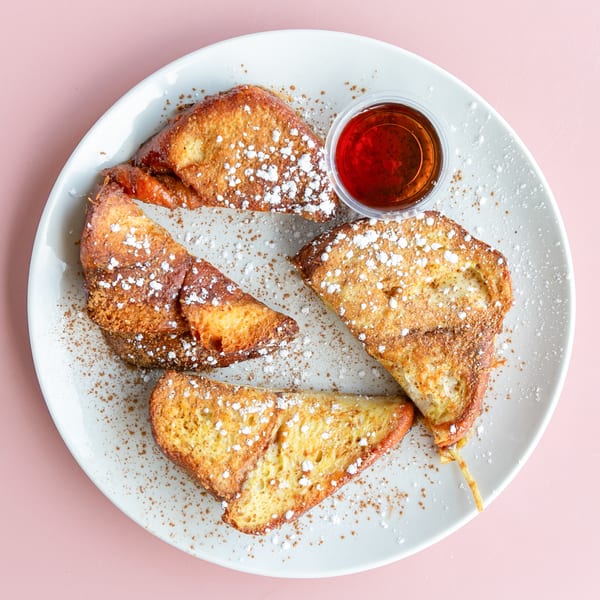 Four pieces of French toast dusted with powdered sugar and cinnamon, with a side of syrup.