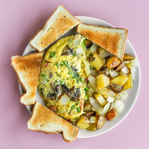 A breakfast plate with a vegetable omelet, home fries, and four pieces of toast.