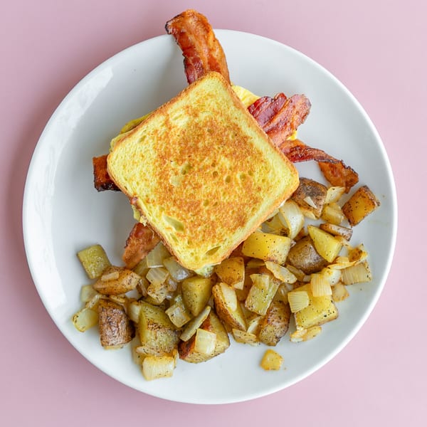 Breakfast sandwich with bacon, egg, and cheese on toasted bread, served with roasted potatoes and onions.